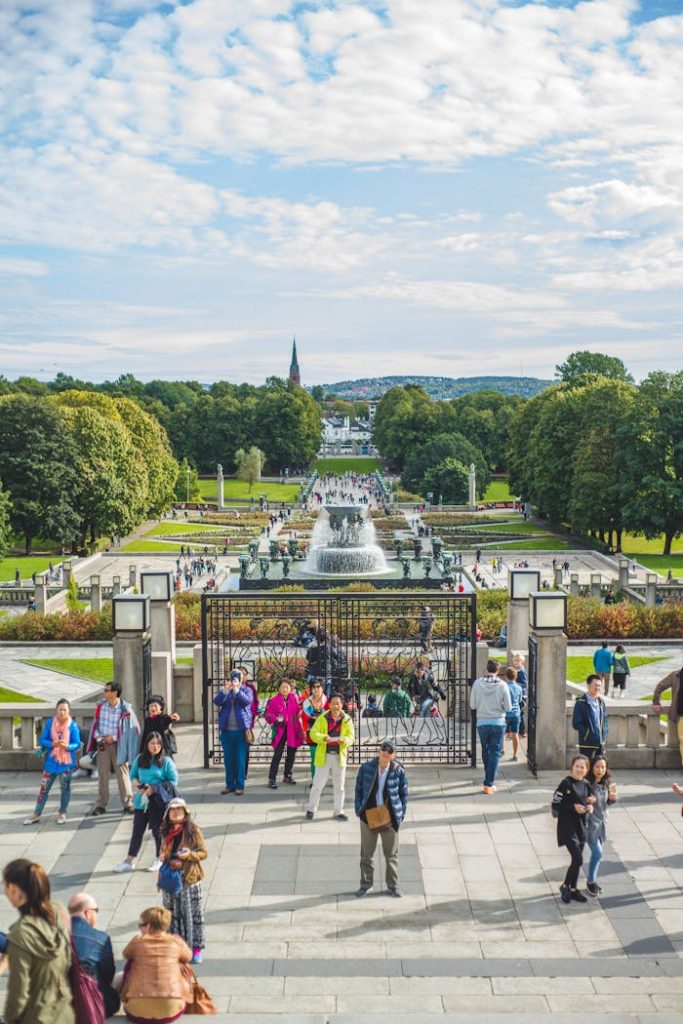 People enjoying a sunny day at Vigeland Park in Oslo, Norway, surrounded by lush greenery and fountains.